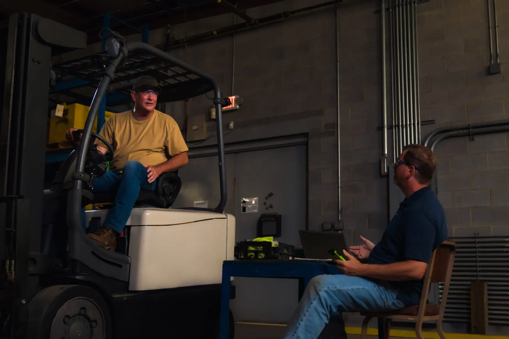 Two men sitting on a forklift in an industrial setting.